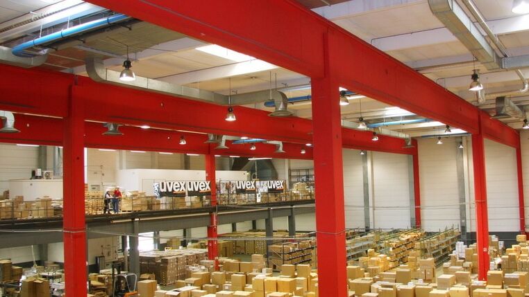 Lagerhalle von Firma Uvex: Blick auf 2 Etagen mit Kartons gerichtet, ein OPTIMA plus Deckenstrahler von KÜBLER hängt über roten Stahlstützleisten