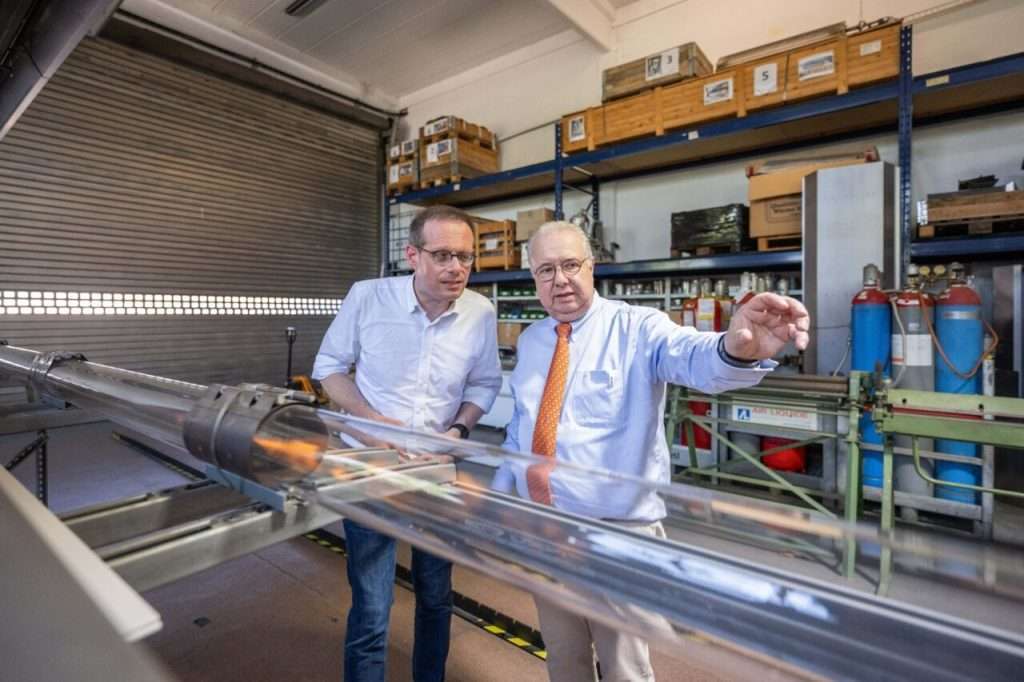 Two men inspect technical equipment in a workshop.