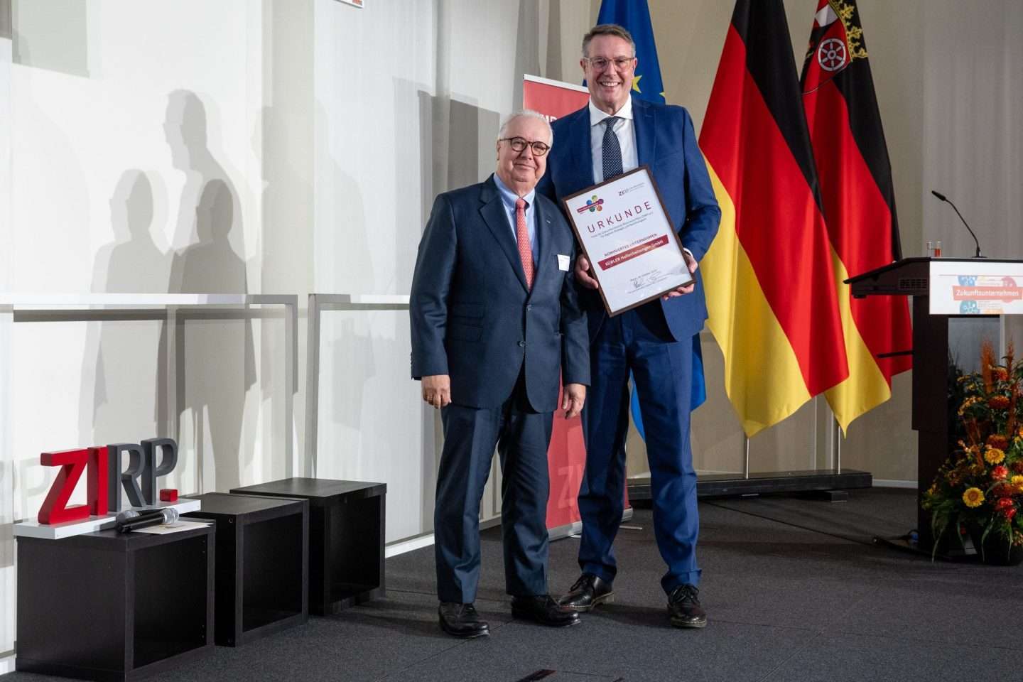 Zwei Männer bei einer Preisverleihung mit Urkunde