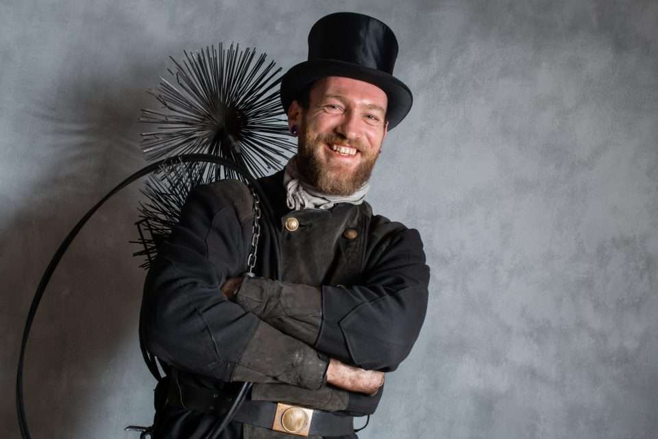 Smilende skorstensfejer med traditionel uniform og værktøj